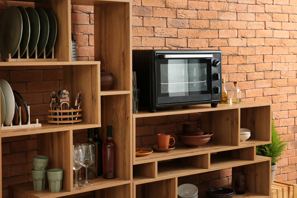 Conjunto de pratos limpos com utensílios e forno de microondas em prateleiras de madeira perto da parede de tijolo
 - Foto, Imagem