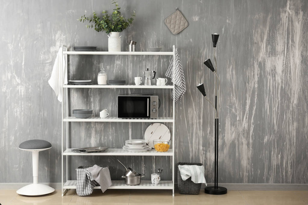 Set di piatti puliti con utensili e forno a microonde sugli scaffali vicino alla parete grigia
 - Foto, immagini
