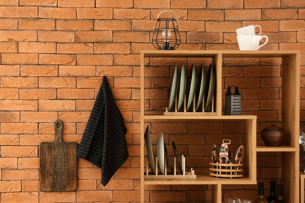 Set di piatti puliti con utensili su scaffali in legno vicino al muro di mattoni
 - Foto, immagini