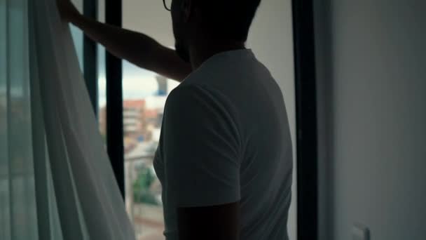 Człowiek wychodzi na balkon mieszkania i biorąc telefon komórkowy w słoneczny dzień - Materiał filmowy, wideo