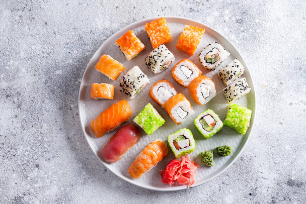 Varios sushi fresco y delicioso establecido en pizarra blanca con palos de madera, salsa sobre fondo de piedra clara, puesta plana
 - Foto, Imagen