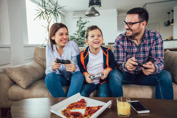 Šťastná rodina sedí na pohovce a hraní počítačových her a stravování - Fotografie, Obrázek