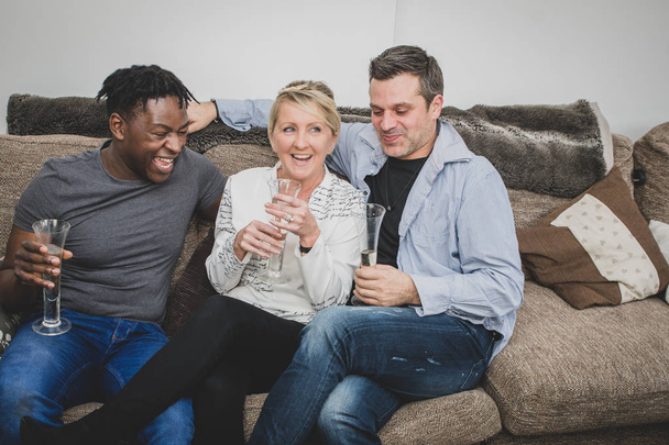Um casal gay interracial, com família extensa, sentado em um sofá em casa e comemorando com uma taça de champanhe. Negros, caucasianos e mestiços
.  - Foto, Imagem