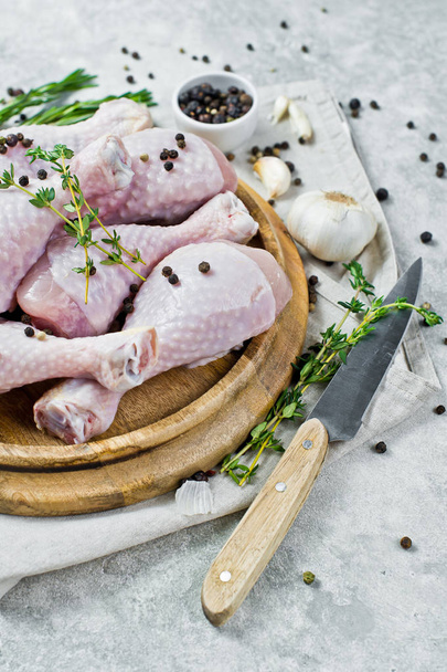 Raw chicken legs. Ingredients for cooking: rosemary, thyme, garlic, pepper. Gray background, side view. - Foto, Imagem