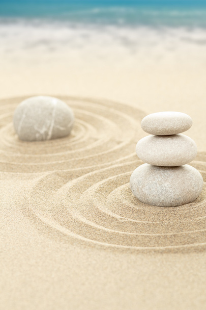 Equilíbrio de pedras zen na areia com o mar no fundo
 - Foto, Imagem