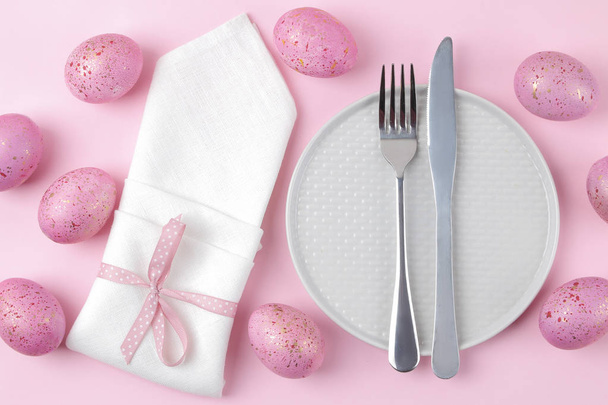 Пасха. Розовые пасхальные яйца и тарелки, нож и вилка на модном розовом фоне. Накрытие пасхального стола. Счастливой Пасхи. праздники. вид сверху
 - Фото, изображение