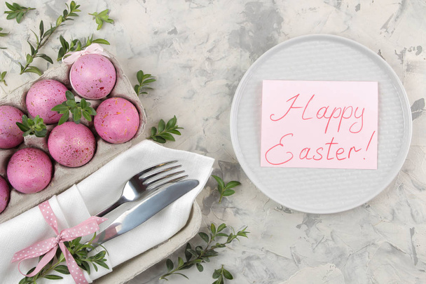 Πάσχα. Ροζ αυγά του Πάσχα και ένα μαχαίρι με ένα πιρούνι και ένα πιάτο σε ανοιχτόχρωμο φόντο σκυροδέματος. Ρύθμιση πίνακα Πάσχας. Καλό Πάσχα. διακοπές. το top view. - Φωτογραφία, εικόνα