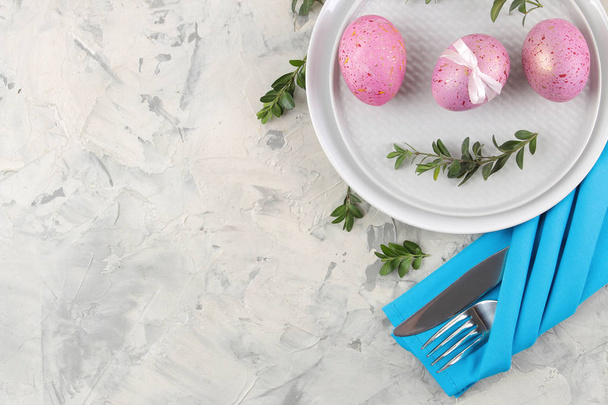 Πάσχα. Ροζ αυγά του Πάσχα και ένα μαχαίρι με ένα πιρούνι και ένα πιάτο σε ανοιχτόχρωμο φόντο σκυροδέματος. Ρύθμιση πίνακα Πάσχας. Καλό Πάσχα. διακοπές. το top view. - Φωτογραφία, εικόνα