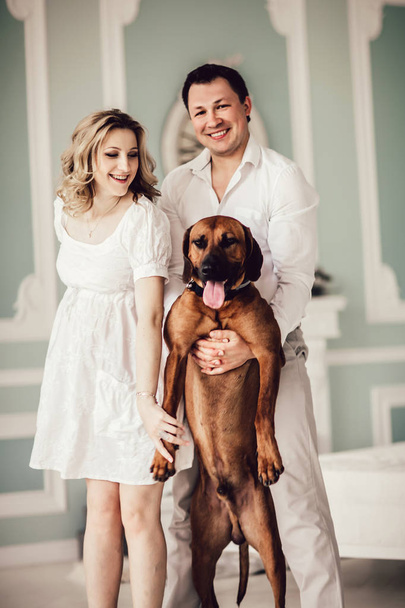 happy young couple and their favorite dog standing in the living room. - Foto, Bild