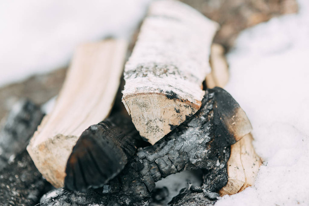 Stack of birch wood in the snow. Extinguished fire and coals on the boards. - Фото, зображення