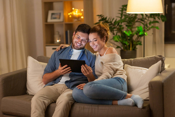 happy couple using tablet pc at home in evening - Foto, imagen
