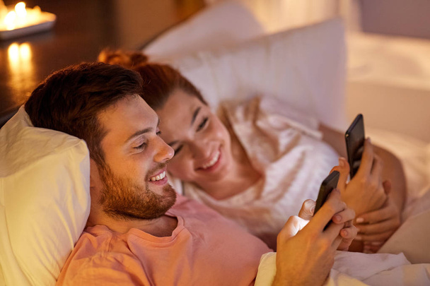 happy couple using smartphones in bed at night - Фото, зображення