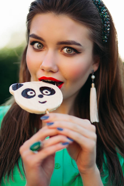 Retrato de la hermosa chica morena en vestido verde, comiendo dulces como panda
. - Foto, Imagen