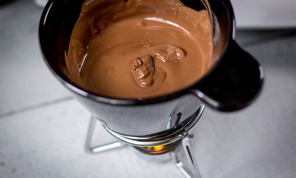Μικρό μαύρο κουβά με λιωμένη σοκολάτα γάλακτος - Φωτογραφία, εικόνα