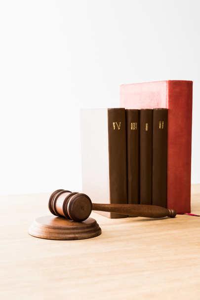 brown gavel near row of red and brown books on wooden table isolated on white - Foto, Imagen