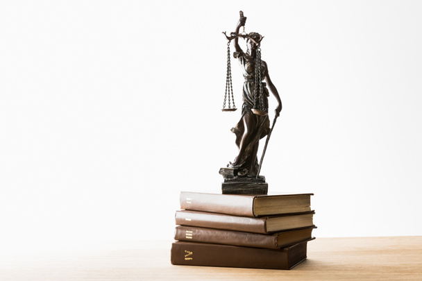 bronzen beeldje met schubben van Justitie op stapel bruin boeken op houten tafel geïsoleerd op wit - Foto, afbeelding