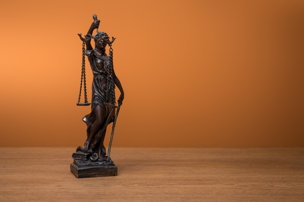 Turuncu zemin üzerine ahşap masa üzerinde adaletin terazisi ile bronz heykelciği - Fotoğraf, Görsel