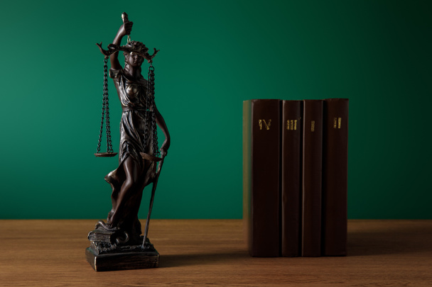bronze statuette with scales of justice and volumes of brown books on wooden table on dark green background - Photo, Image