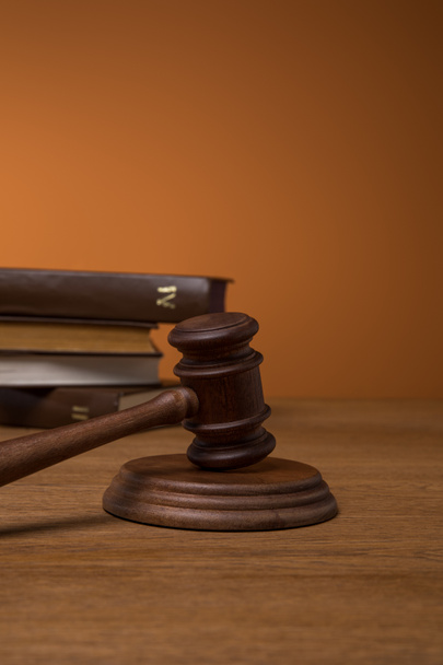selective focus of volumes of brown books in leather covers and gavel on wooden table on dark orange background - Photo, Image