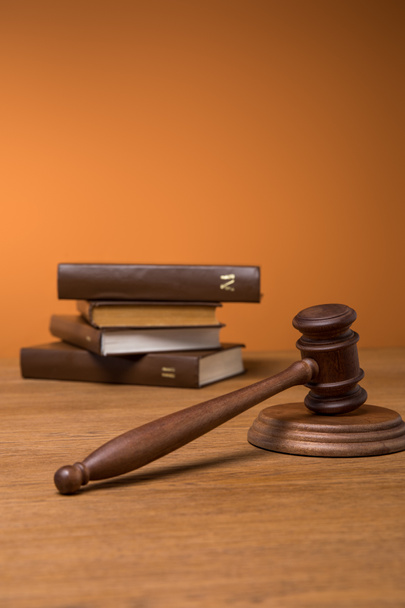 selective focus of volumes of brown books in leather covers and gavel on wooden table on orange background - Photo, Image