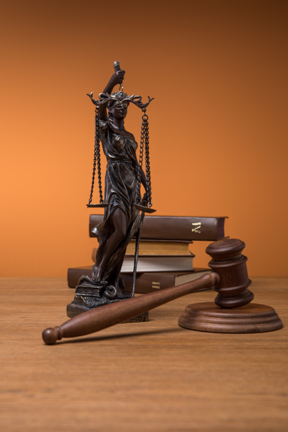 Bronzestatuette mit Gerechtigkeitswaage, Hammer und Büchern auf Holztisch auf orangefarbenem Hintergrund - Foto, Bild
