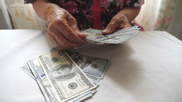 Großmutter hält Bargeld in der Hand und zählt Fremdwährungen über den Tisch. Arme einer alten Frau betrachten Hundert-Dollar-Scheine über dem Schreibtisch. Geldkonzept. Ansicht von oben Nahaufnahme Zeitlupe - Filmmaterial, Video