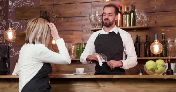 Barkeeper putzt ein Glas und hört seiner Mitarbeiterin sehr konzentriert zu - Filmmaterial, Video