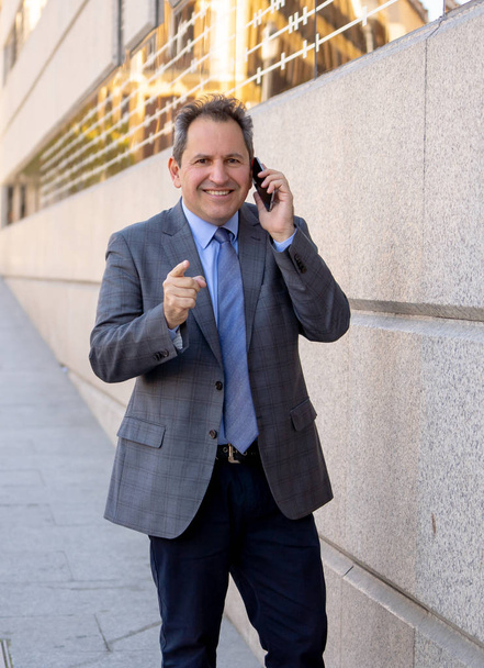 Porträt eines hübschen Geschäftsmannes mittleren Alters, der durch die Stadt läuft und mit dem Handy telefoniert - Foto, Bild
