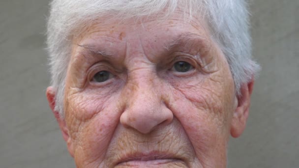 Portret van oude grootmoeder met een triest gezicht. Gerimpeld gezicht van oudere dame op zoek naar de camera. Verdriet gelaatsuitdrukking van oma. Close-up van de blik van rijpe vrouw - Video