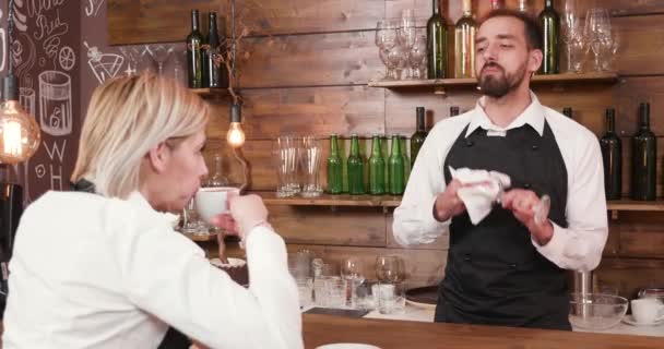 Mannelijke barman praat met de serveerster tijdens het schoonmaken van een glas - Video