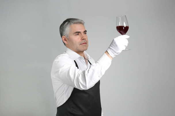 Mature sommelier with glass of wine on grey background - Photo, Image