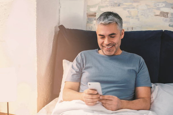 Зрелый мужчина с мобильным телефоном в постели
 - Фото, изображение