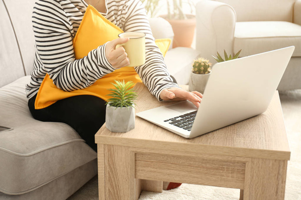 Jonge vrouw met laptop en drinken koffie thuis - Foto, afbeelding
