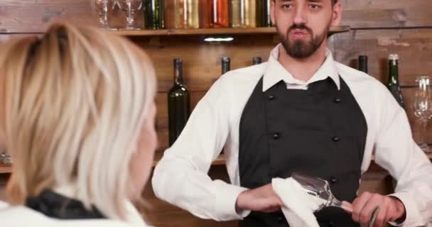 Красивий чоловік бармен розмовляє зі своїм колегою і чистить скло
 - Кадри, відео