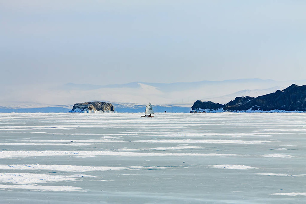Ice boat rides on the ice of Lake Baikal in the background Olkhon in the winter foggy morning away - Photo, image
