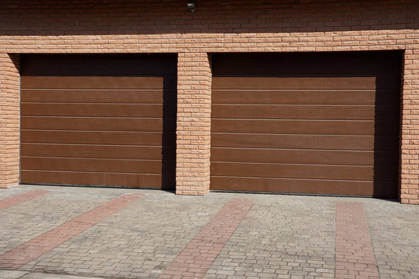 fachada de un garaje de ladrillo marrón con dos puertas en la calle
 - Foto, Imagen