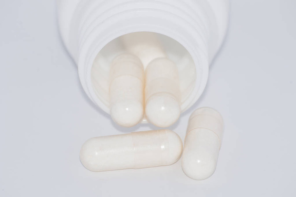 Pilules blanches sur fond blanc tombent d'un pot en plastique
. - Photo, image