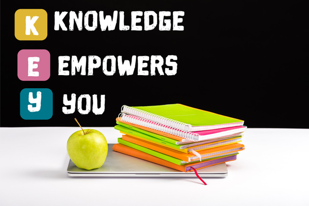 closed laptop, green apple, notebooks and color pencils on desk with knowledge empowers you lettering on black  - Photo, Image