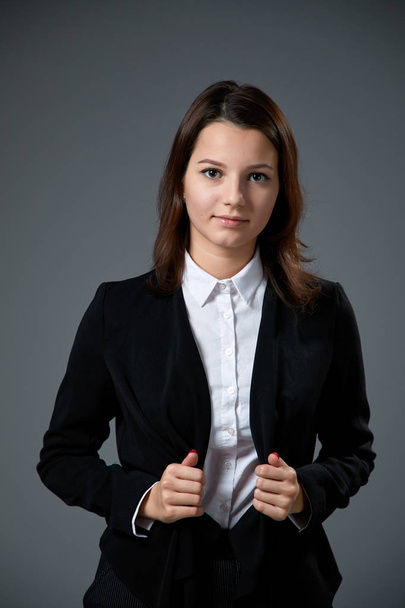 Porträt einer schönen jungen Frau in weißem Hemd und schwarzer Jacke, die auf grauem Hintergrund posiert   - Foto, Bild