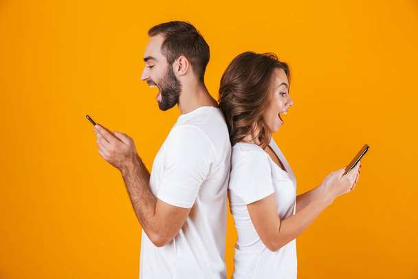 Image of happy couple smiling while both using smartphones, isol - Zdjęcie, obraz