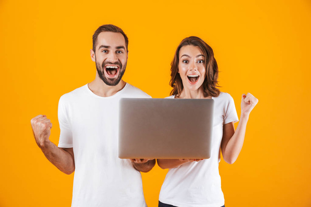 Portrait of joyous man and woman holding silver laptop, while st - Фото, изображение