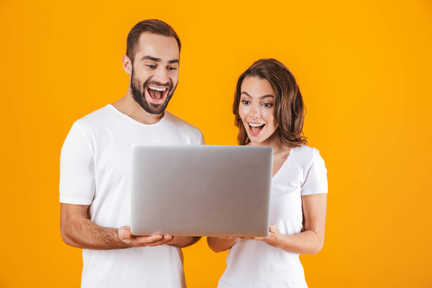 Portrait of positive man and woman holding silver laptop, while  - Foto, afbeelding