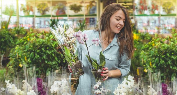 Kaunis naispuolinen asiakas tuoksuva värikäs kukkivat orkideat vähittäiskaupassa
.  - Valokuva, kuva