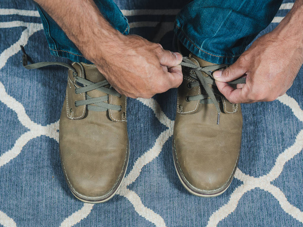 Kot pantolonlu bir adam kahverengi deri ayakkabılarla ayakkabı bağını bağlıyor.  - Fotoğraf, Görsel