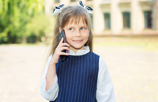 Call your parents. Girl schoolgirl talking on mobile phone in front of school. - Zdjęcie, obraz