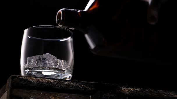 Whiskey pouring in the glass from the bottle. With ice cubes. - Video