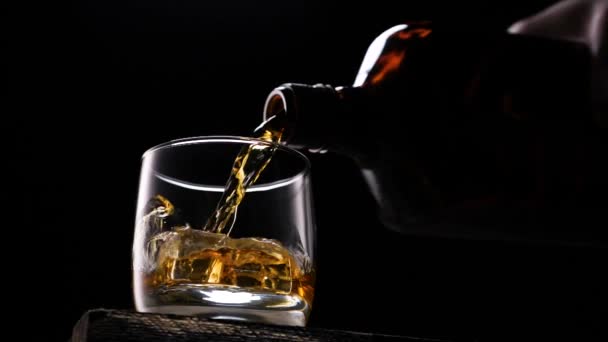 Whiskey pouring in the glass from the bottle. With ice cubes. - Imágenes, Vídeo