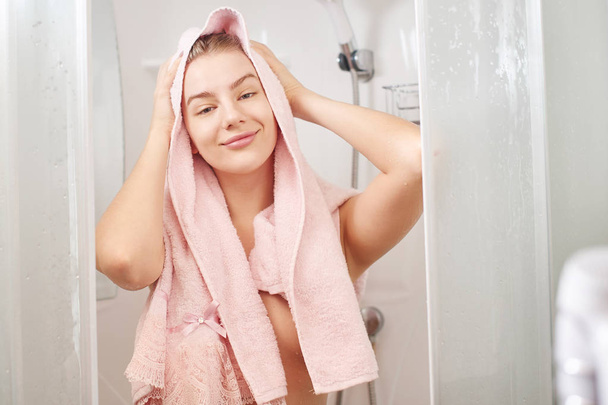 A beautiful blonde woman took a shower, washed her hair and wipe them with pink towel, smile and a satisfied face in the bathroom. - Foto, afbeelding