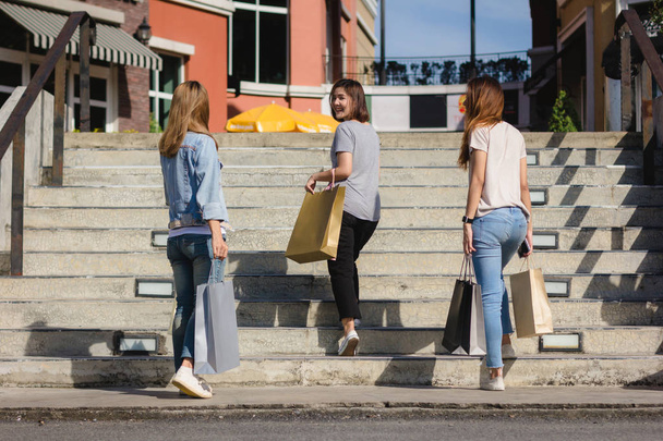 Gruppe junger asiatischer Frauen beim Einkaufen auf einem Outdoor-Markt mit Einkaufstaschen in der Hand. junge asiatische Frauen zeigen unter warmem Sonnenlicht, was sie in der Einkaufstasche haben. Gruppe Outdoor-Shopping-Konzept. - Foto, Bild