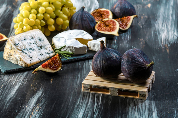 Cheese plate served with grapes, figs and nuts on a black background. Food background. Top view. Copy space - Valokuva, kuva